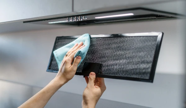Woman cleaning aluminum mesh filter wipe dirty part of black metal kitchen hood