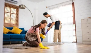Young man and woman cleaning house indoors together happy couple vacuuming messy dirty floor for housekeeping
