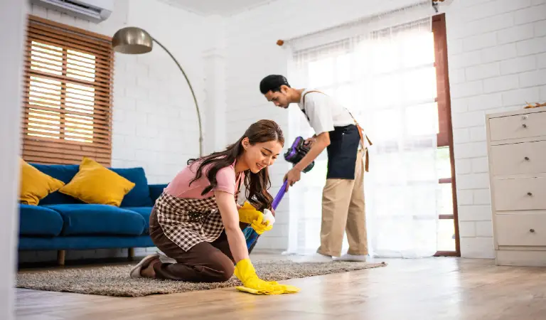 Young man and woman cleaning house indoors together happy couple vacuuming messy dirty floor for housekeeping