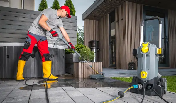 Caucasian worker power washing patio concrete bricks using professional pressure washer