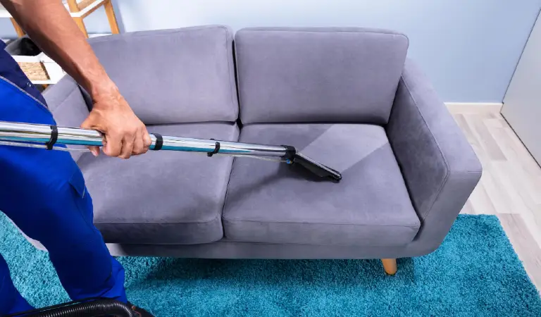Man cleaning sofa with vacuum cleaner