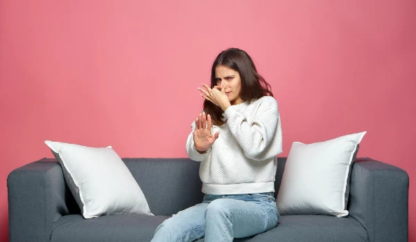 Bad smell young girl pinch nose showing stop gesture feel disgust sitting on sofa suffering parosmia