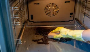 Hand in rubber glove cleaning dirty oven with sponge and cleaner housework and housekeeping concept