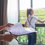 Midsection of woman looking at clipboard against colleague cleaning window