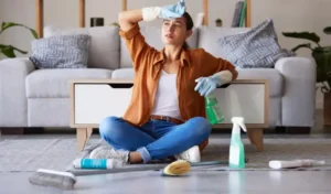 Tired woman cleaning and sitting on living room floor with detergent chemicals or sanitizer spray for hygiene at home