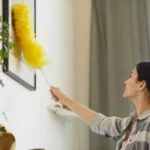 Young woman working at home she wiping dust from pictures on the wall
