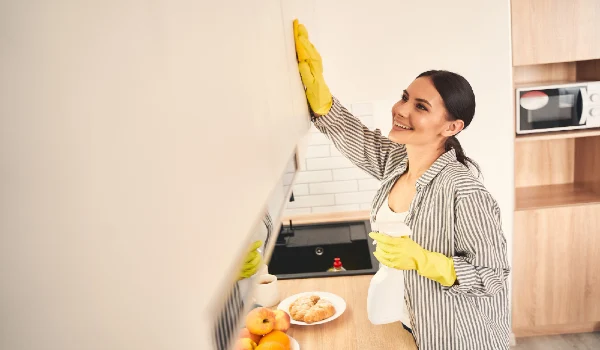 Be positive. Delighted young female standing in semi position and cleaning furniture with pleasure