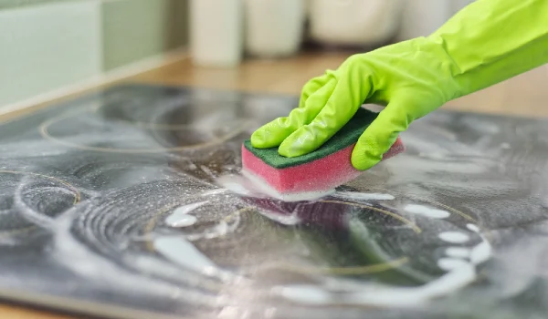 Woman hands in gloves cleans kitchen electric ceramic hob with sponge