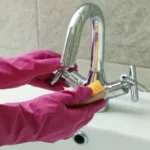 Woman in rubber pink glove cleaning sink chrome tap
