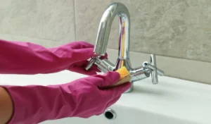 Woman in rubber pink glove cleaning sink chrome tap